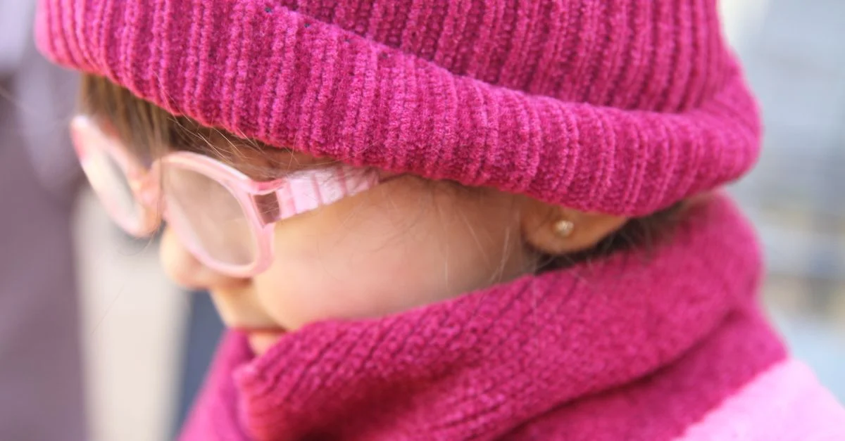 Gros plan d'un enfant portant un chapeau et une écharpe roses en hiver, créant un look saisonnier chaleureux.