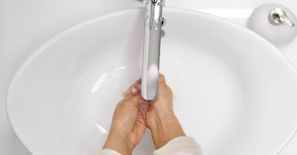 Une femme se lavant les mains sous un robinet chrome dans un évier blanc, mettant l'accent sur l'hygiène.