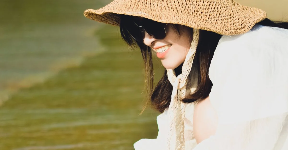Femme souriante portant un chapeau de soleil profitant d'une journée ensoleillée au bord de la mer.