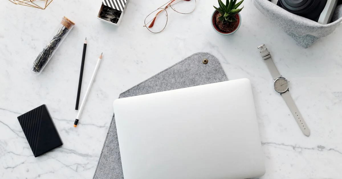 Vue de dessus d'un espace de travail minimaliste avec un ordinateur portable, un appareil photo et des accessoires de bureau sur une surface en marbre.