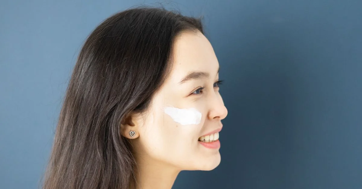 Profil d'une femme avec de la crème sur la joue contre un fond bleu, mettant en avant la routine de soins de la peau.