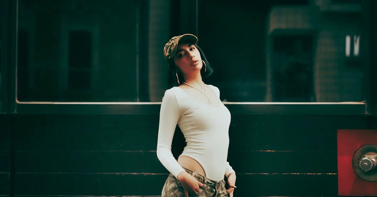 Une femme élégante pose avec assurance en tenue streetwear urbaine sur fond sombre, affichant un style moderne.