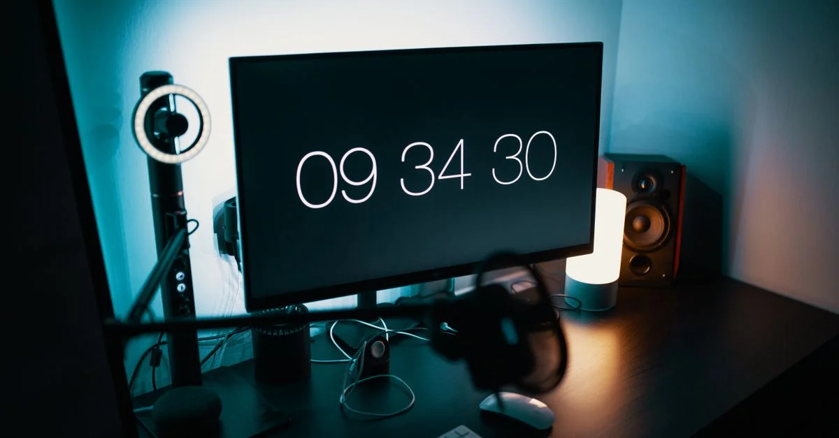 Un bureau élégant avec un grand moniteur, une horloge numérique et un éclairage ambiant.