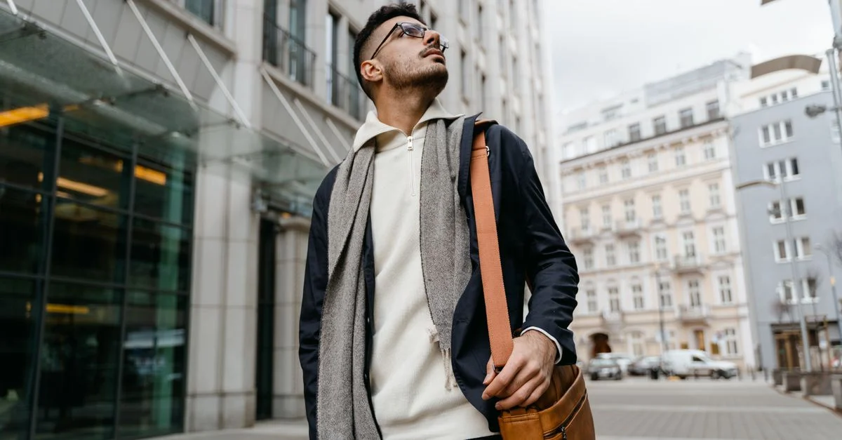 Homme tendance avec un sac en cuir se tenant avec assurance dans un environnement urbain.