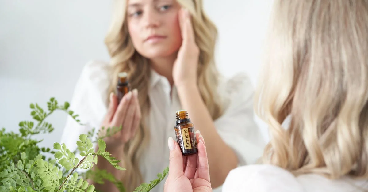 Une femme applique de l'huile naturelle pour le visage devant un miroir, entourée de plantes vertes.
